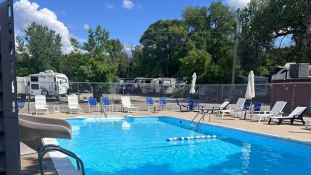 A swimming pool with lounge chairs and umbrellas, surrounded by trees and RVs. - RV Bunkhouse on the River (Mason City)