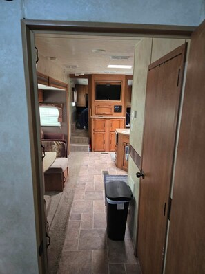 A compact RV interior with a kitchenette, a TV mounted above the counter, and a small trash bin. - RV Bunkhouse on the River (Mason City)