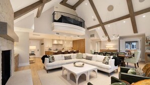 A spacious living area with a large sectional sofa, a fireplace, and a dining area with a high ceiling and exposed beams. - Arrabelle Premier Penthouse - ski in/ski out (Lionshead)