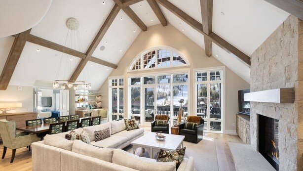 A spacious loft-style living area with a fireplace, large windows, and a dining area. - Arrabelle Premier Penthouse - ski in/ski out (Lionshead)