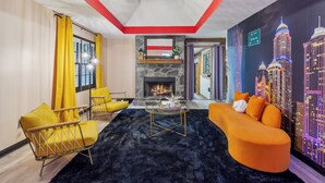 A modern living room with a fireplace, yellow and orange furniture, and a cityscape mural. - Near AtL, Pickleball, Golf, Pool, Karaoke, Tikibar, 1.25 Acre Private Retreat (Locust Grove)