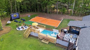 A backyard with a swimming pool, a tennis court, and a deck area with outdoor seating. - Near AtL, Pickleball, Golf, Pool, Karaoke, Tikibar, 1.25 Acre Private Retreat (Locust Grove)