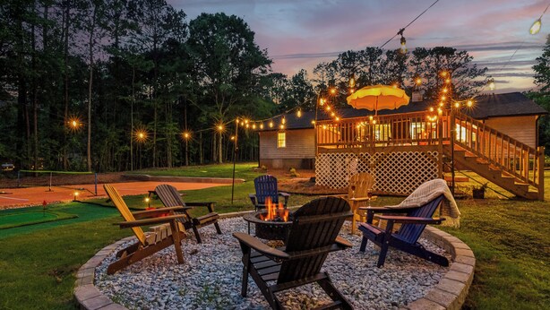 A backyard with a fire pit, outdoor seating, and a deck with string lights. - Near AtL, Pickleball, Golf, Pool, Karaoke, Tikibar, 1.25 Acre Private Retreat (Locust Grove)
