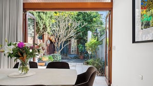 A dining area with a table and chairs, a vase with flowers, and a view of a garden through an open door. - Stylish 3BR, 2BA King Beds Balmain Terrace Near Parks, Ferries & Darling Street (Balmain)