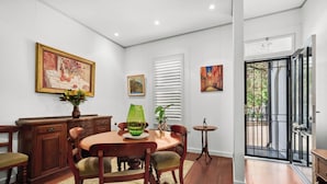 A dining area with a wooden table and chairs, a vase with flowers, and a painting on the wall. - Stylish 3BR, 2BA King Beds Balmain Terrace Near Parks, Ferries & Darling Street (Balmain)