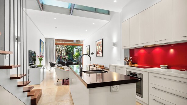 A modern kitchen with a central island, white cabinetry, and a red accent wall. - Stylish 3BR, 2BA King Beds Balmain Terrace Near Parks, Ferries & Darling Street (Balmain)