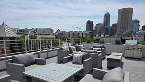 Eine Dachterrasse mit Gartenmöbeln, einem Grill und einer Skyline im Hintergrund.