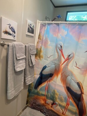 Un bagno con tenda della doccia raffigurante cicogne, asciugamani su un porta asciugamani e opere d'arte incorniciate al muro.