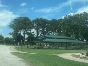 Un parco con un padiglione dal tetto verde, tavoli da picnic e un prato ben curato.
