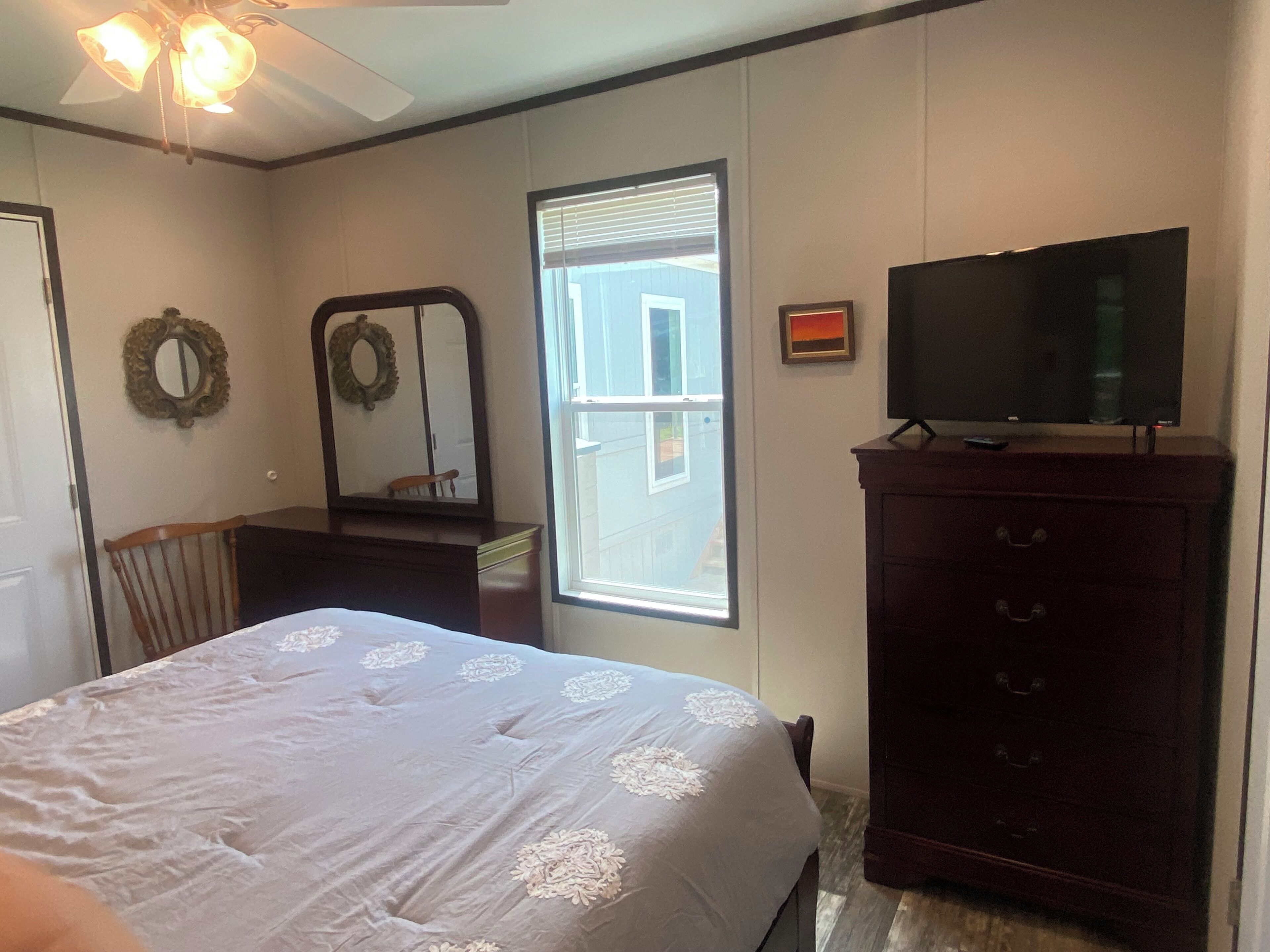 Une chambre à coucher comprenant un lit, une commode, un téléviseur et une fenêtre avec des stores.