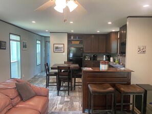 A modern kitchen with dark wooden cabinets, a central island, and a dining area with a brown leather couch and bar stools.