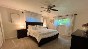 Um quarto com uma cama grande, duas mesas de cabeceira com luminárias, um ventilador de teto e uma janela com cortinas.