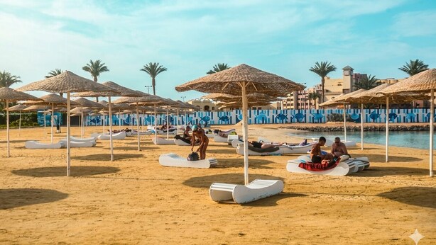 Een strand met ligbedden, parasols, een zwembad en palmbomen.