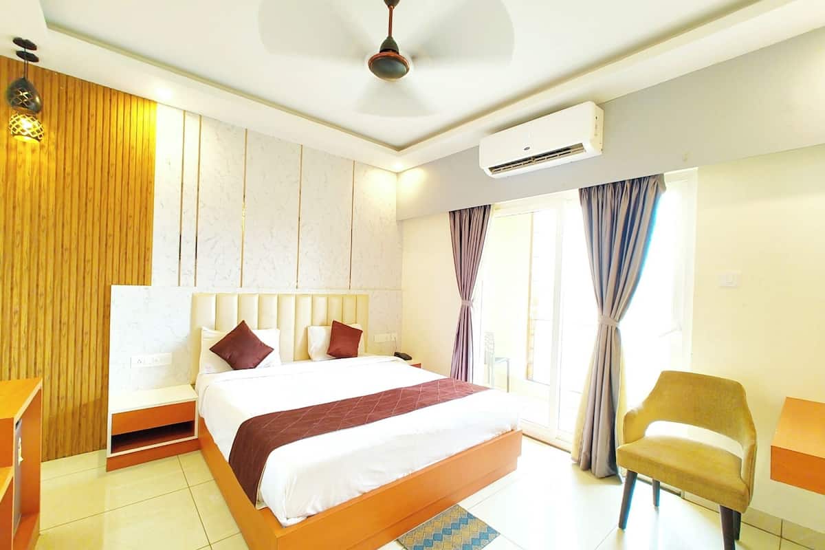 Quarto de hotel com uma cama grande, um ventilador de teto, um aparelho de ar condicionado, parede revestida de painéis de madeira, uma janela com cortinas e uma cadeira.