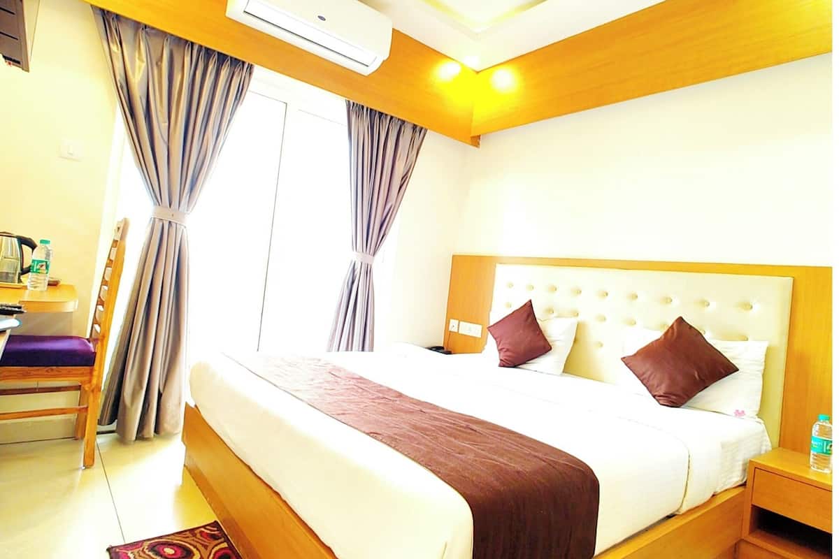 Quarto de hotel com uma cama grande, cabeceira de madeira, mesa de cabeceira, televisão, ar condicionado e janela com cortinas.