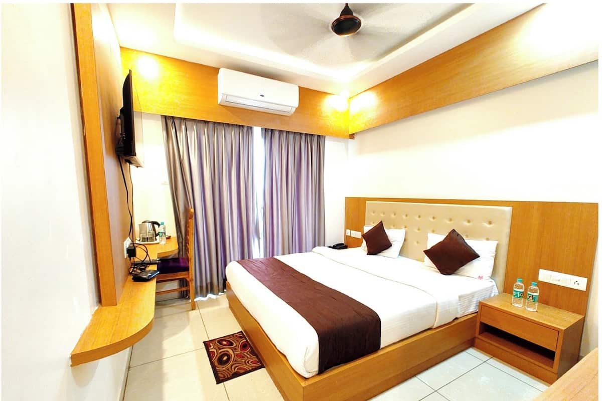 Quarto de hotel com uma cama grande, uma escrivaninha com cadeira, uma televisão de tela plana na parede e um ar condicionado.