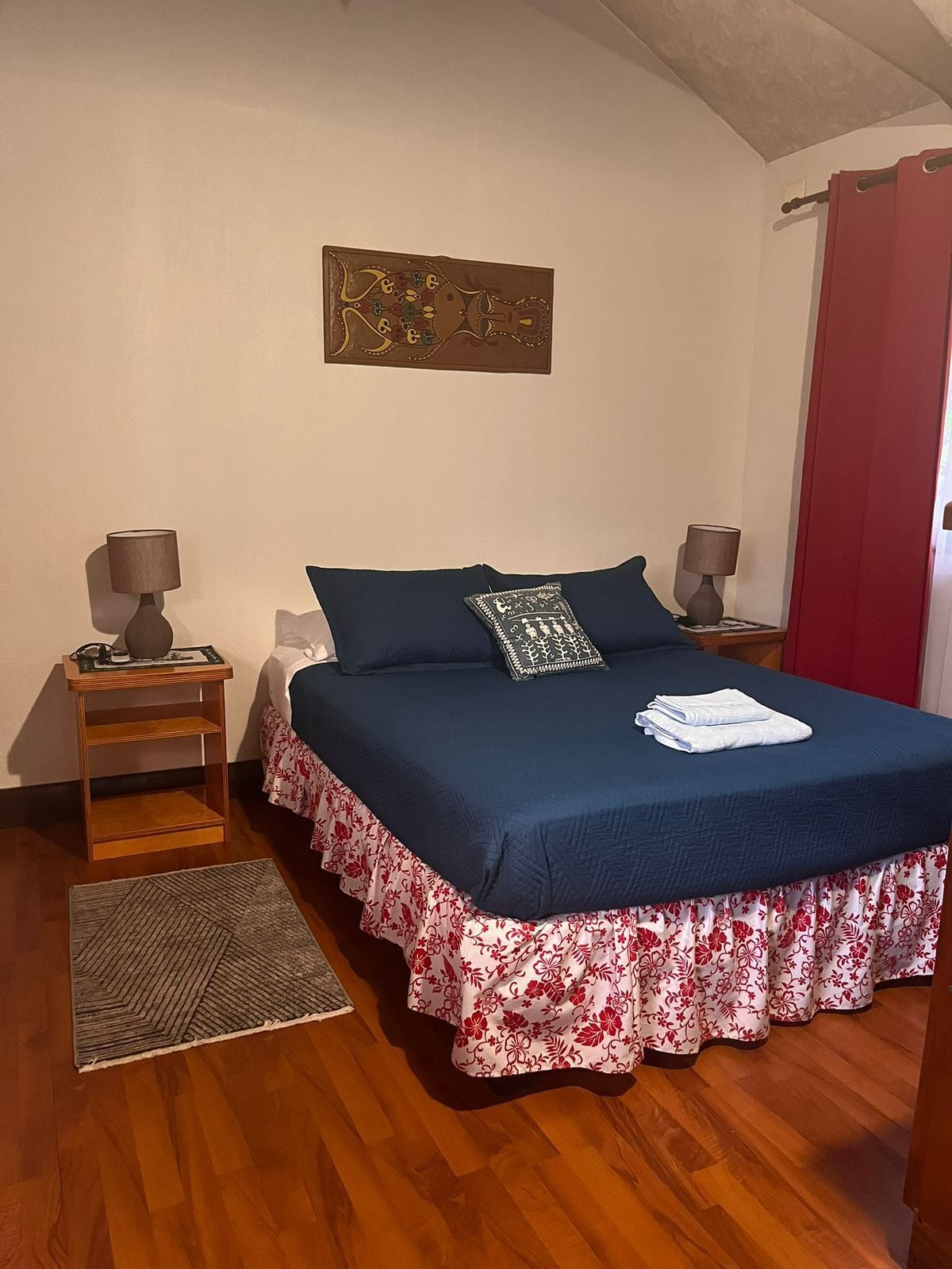A bedroom with a bed, two bedside tables, a rug, and a wall decoration.