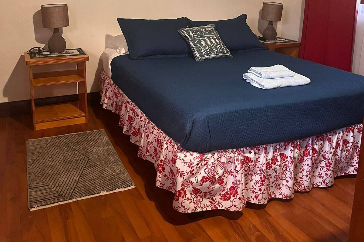 Un dormitorio con una cama, dos mesitas de noche, una alfombra y un adorno en la pared.