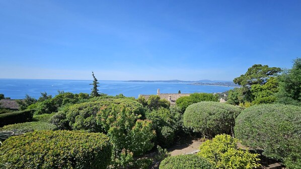 A coastal landscape with a clear view of the sea, lush greenery, and traditional architecture.