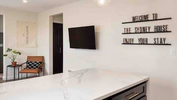 A modern kitchen with a marble countertop, a flat-screen TV, and a welcome sign.