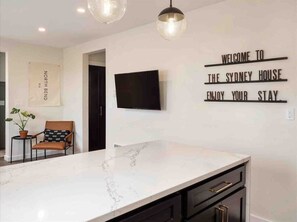 Una cocina moderna con encimera de mármol, un televisor de pantalla plana y un letrero de bienvenida.