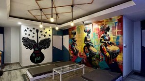 A room with a mural of musical instruments and a guitar with the phrase "let the music be your pilot." There are benches and a small table. - Moustache Hostel Rishikesh (Rishikesh)