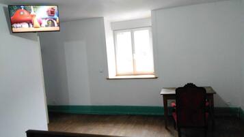 Una habitación con piso de madera, una ventana con persianas, un escritorio pequeño y una silla.