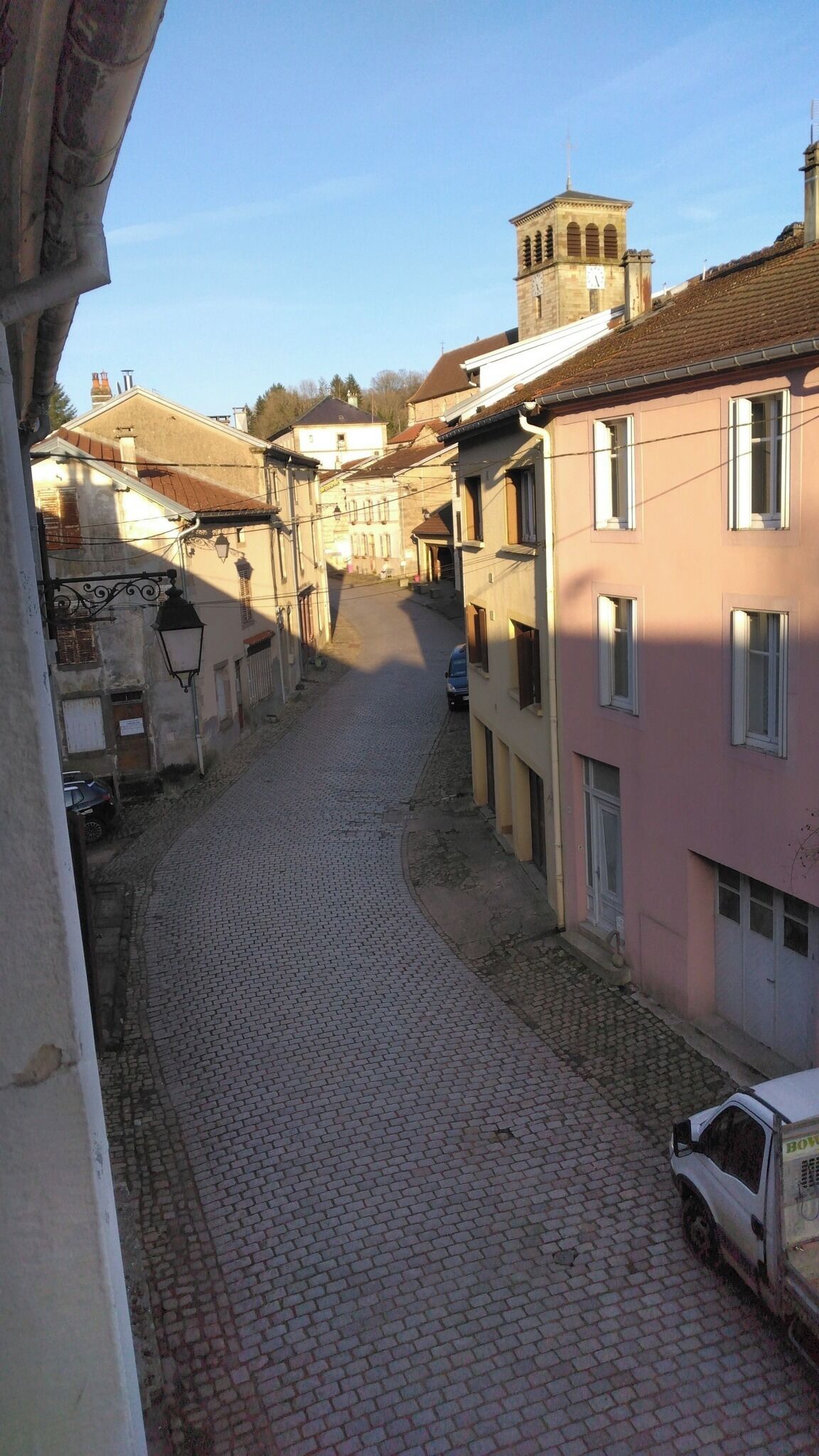 Une rue pavée bordée d’immeubles, une tour de l’horloge et un fourgon garé.