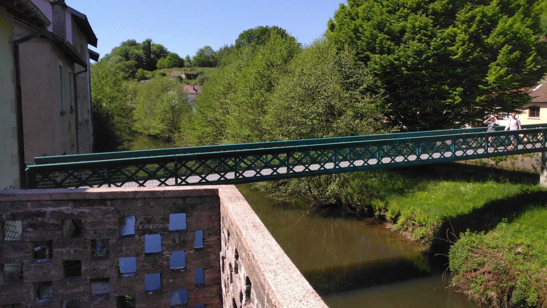 A green bridge over a river with a building on one side and trees in the background.