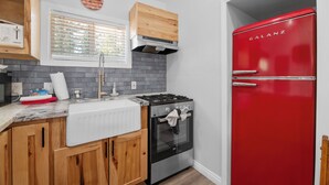 Eine Küche mit Holzschränken, einem roten Kühlschrank, einem Herd und einem Fenster mit Jalousien.