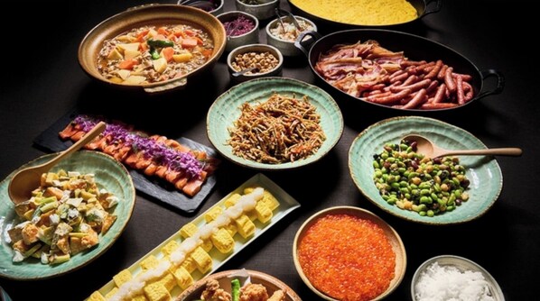 Verschiedene Gerichte, darunter Sushi, Sashimi und andere asiatische Spezialitäten, sind auf einem Tisch angerichtet.