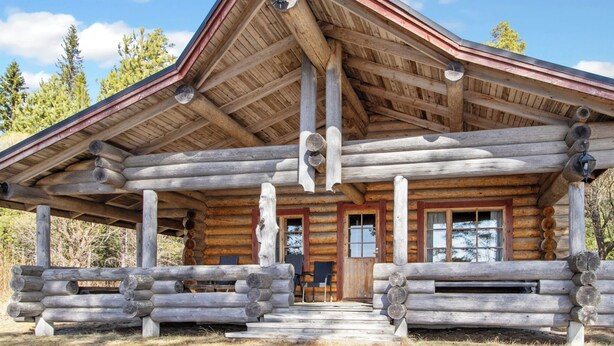 A log cabin with a porch, wooden beams, and a front door.