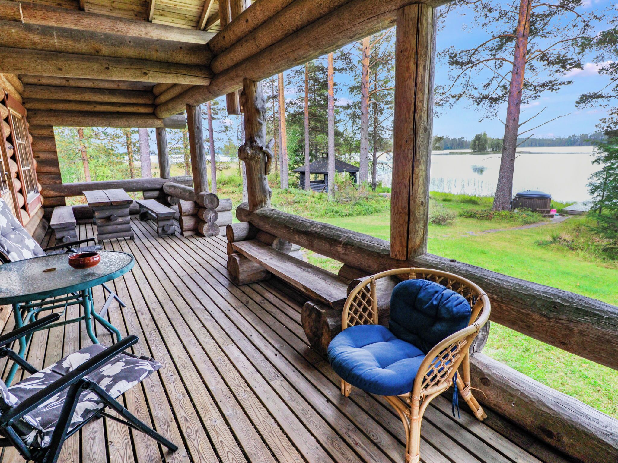 A wooden deck with outdoor furniture, including a table and chairs, overlooking a lake.
