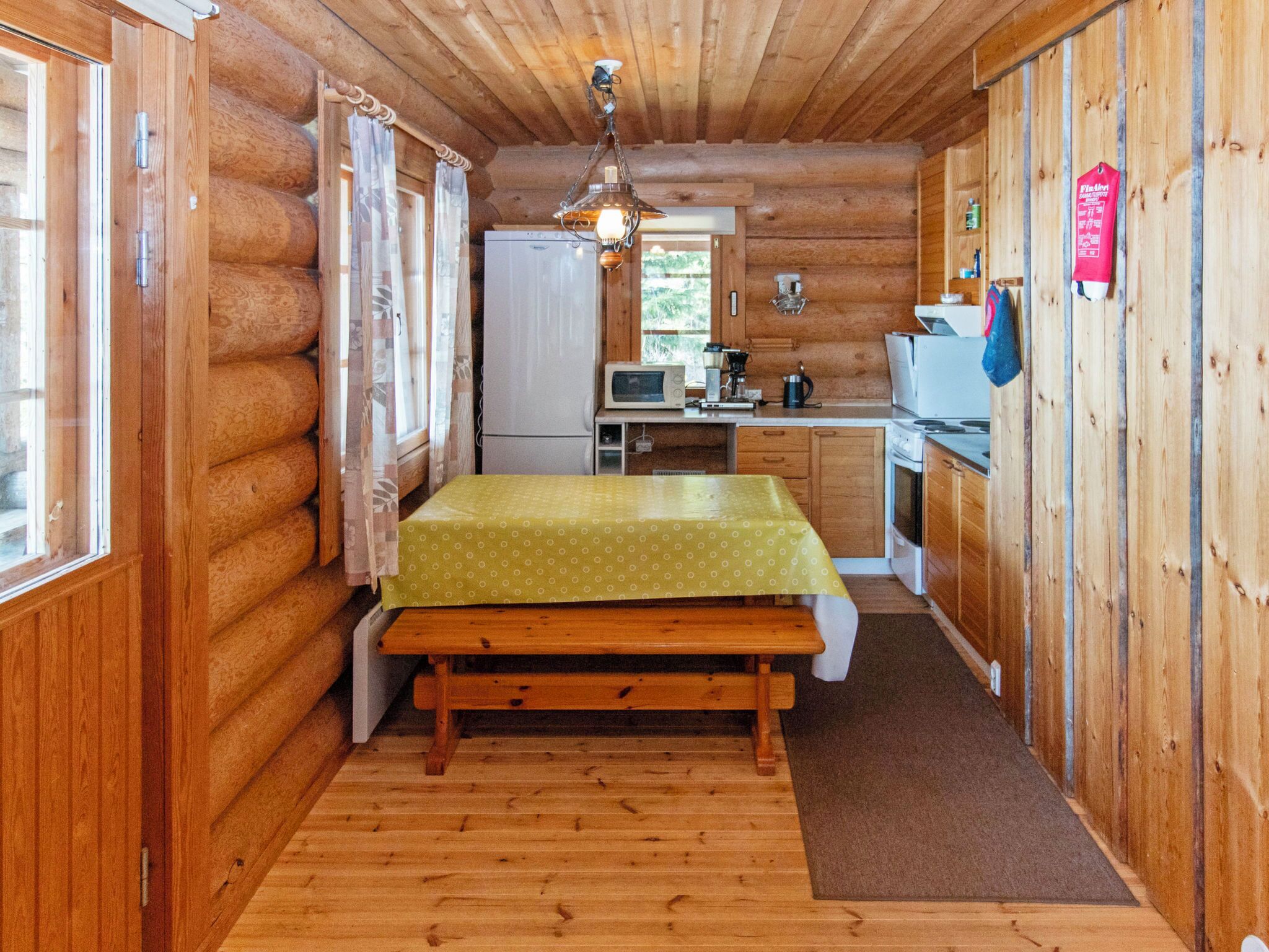 Een knus houten chalet kamertje met een bed, kitchenette en een eettafeltje.
