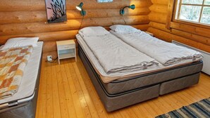 A cozy log cabin bedroom with a double bed, a small bedside table, a lamp, and a window with a view of trees.