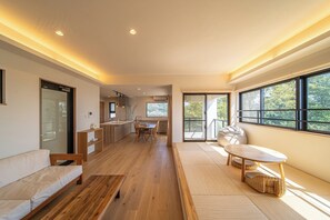 A modern interior with a wooden floor, a sofa, a dining table, and a view through large windows.