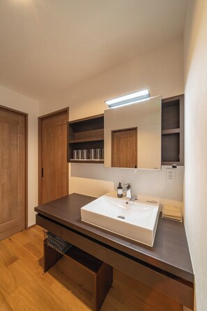 Een moderne badkamer met een witte wastafel, houten kastjes en een spiegel boven de wastafel.