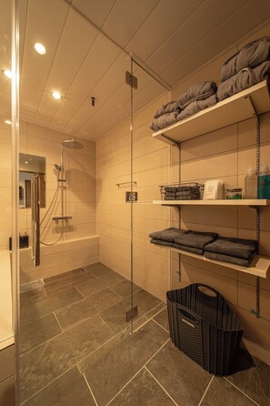 Een badkamer met een douchecabine van glas, betegelde vloer en planken met handdoeken en toiletartikelen.