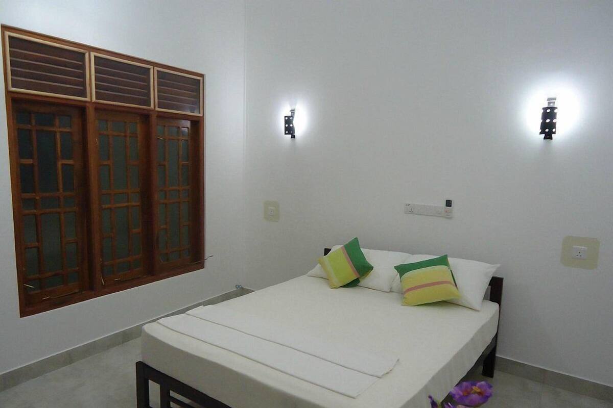 Une chambre à coucher avec un lit, deux lampes fixées au mur, une fenêtre avec des volets en bois et une petite table de chevet.