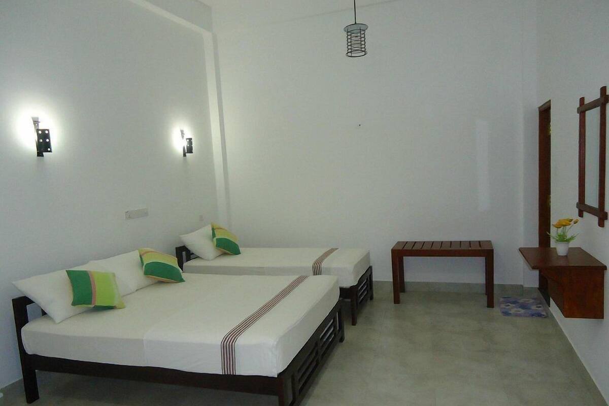Une chambre d’hôtel avec deux lits, une petite table, un banc et un miroir.
