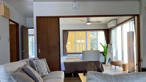 Un salon moderne avec un canapé, une table basse et un coin repas. Il y a une grande fenêtre avec des rideaux, un ventilateur de plafond et un appareil de climatisation.