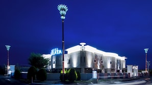 Un hotel moderno con un letrero llamativo, una entrada bien iluminada y un área de estacionamiento.