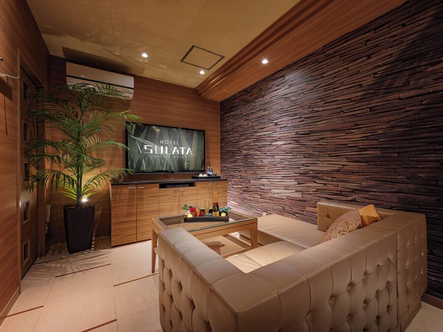 A modern hotel room with a wooden wall, a flat-screen TV, a sofa, and a coffee table with a bottle of champagne.