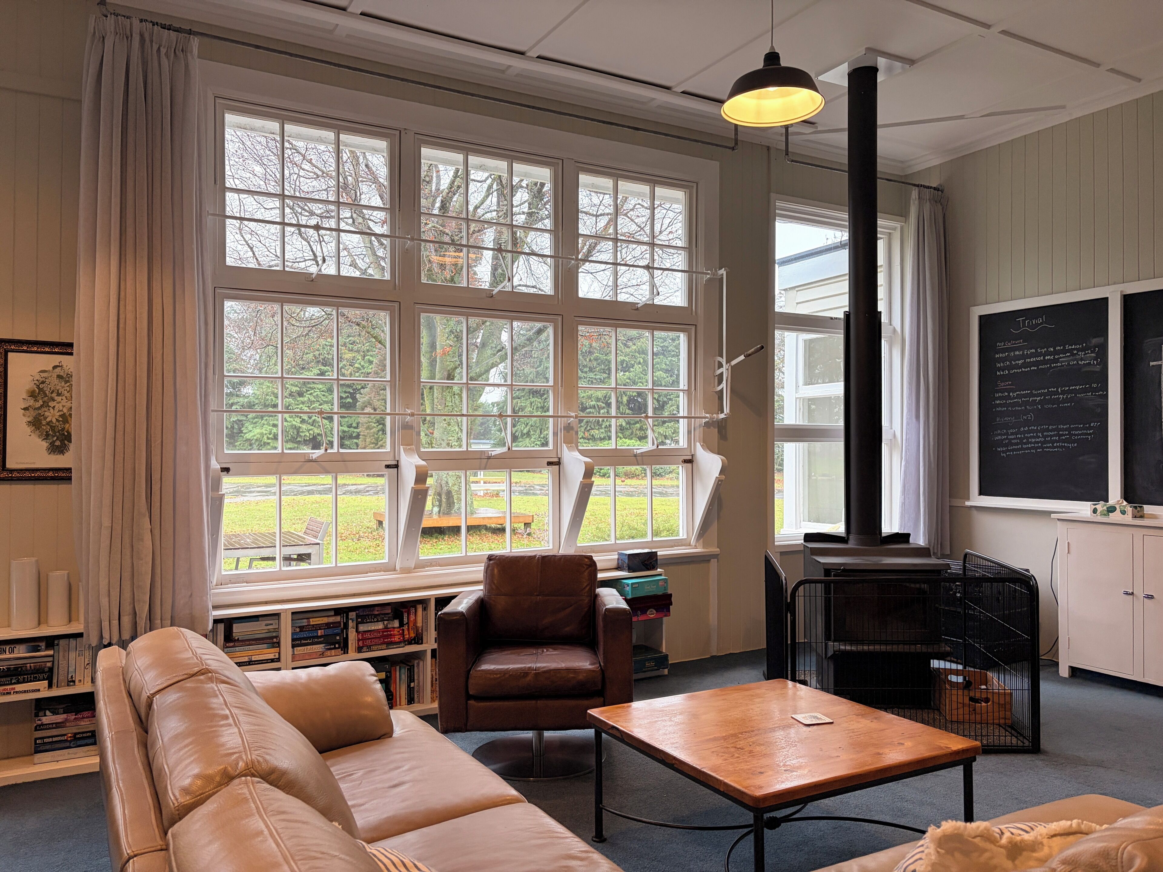 A room with a large window, a sofa, a chair, a table, a bookshelf, and a blackboard.