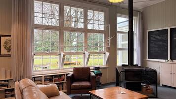 A room with a large window, a sofa, a chair, a table, a bookshelf, and a blackboard.
