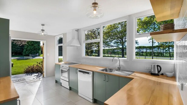 Una cocina moderna con encimera de madera, electrodomésticos de acero inoxidable y ventanas amplias con vistas a un paisaje verde.