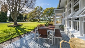 Una terraza de madera con una mesa y sillas, rodeada de un césped cuidado y árboles.