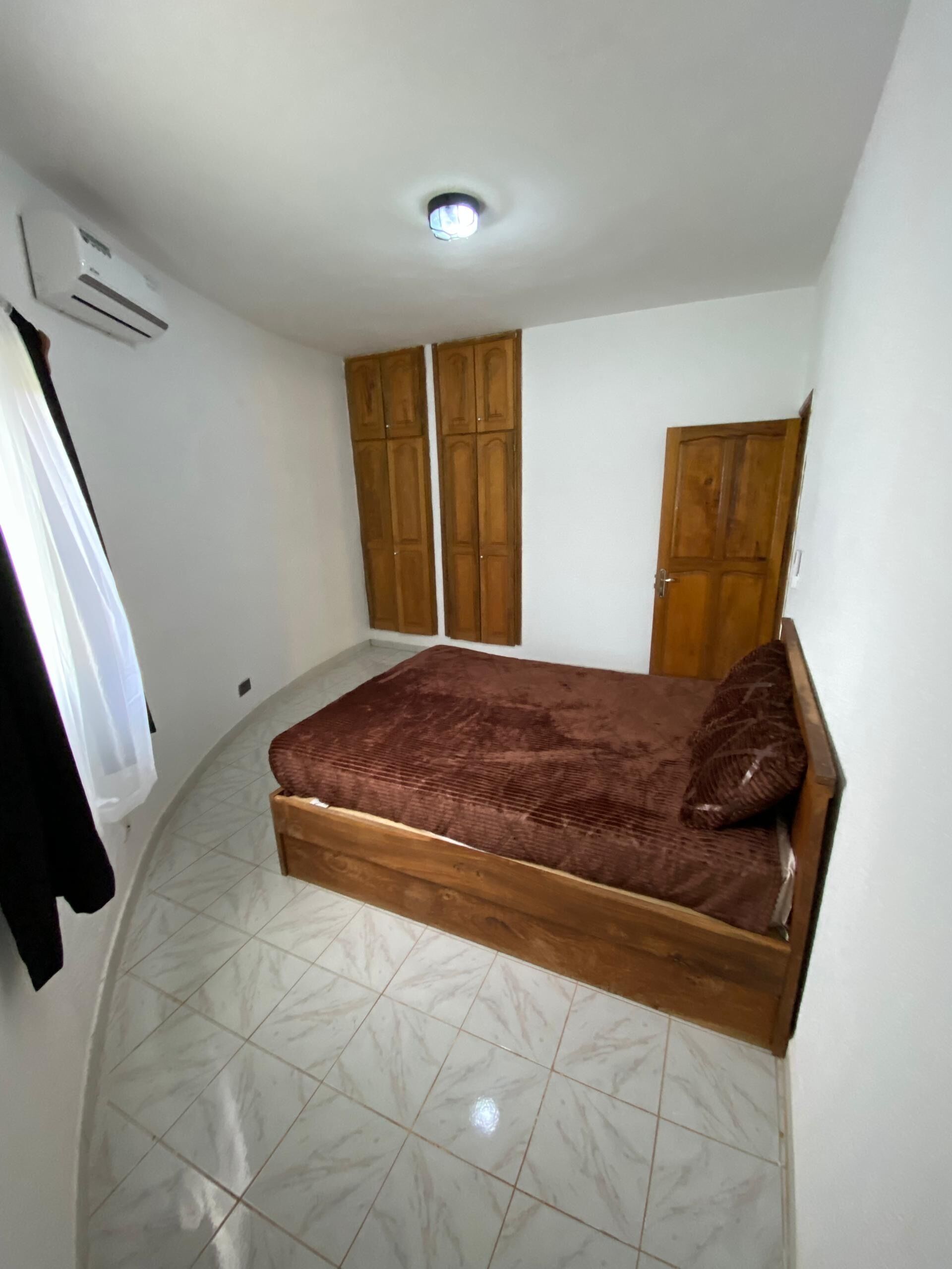 A bedroom with a bed, wardrobe, and an air conditioning unit.