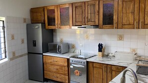 A kitchen with wooden cabinets, a refrigerator, a microwave, a stove, and a sink. - Charming 3-bedroom villa with Wifi, AC in lovely Somone near Saly. (Somone)