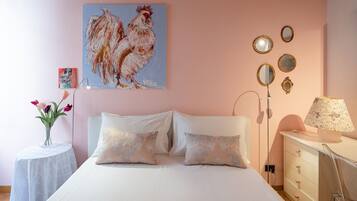 Une chambre à coucher avec un lit, des oreillers, une table de chevet avec une lampe, une commode, un miroir et un tableau accroché au mur.